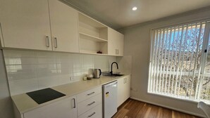A modern kitchen with white cabinets, a built-in dishwasher, and a window with blinds. - Guest Suite Bredbo (Jerangle)