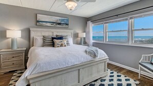 A bedroom with a bed, nightstands, a ceiling fan, a window with a view, and a chair. - Amelia South F1 - Hosted by Moore AI Rentals (Fernandina Beach)