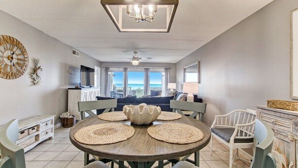 A dining area with a round table, woven placemats, and a chandelier. - Amelia South F1 - Hosted by Moore AI Rentals (Fernandina Beach)