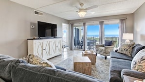 A spacious living room with a grey sofa, a white cabinet with a flat-screen TV, and a ceiling fan. - Amelia South F1 - Hosted by Moore AI Rentals (Fernandina Beach)