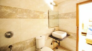 A bathroom with marble walls, a toilet, a sink, and a mirror. - Hotel Lav Kush Deluxe (New Delhi)