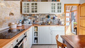 A kitchen with white cabinets, a stone wall, a wooden countertop, and a sink.