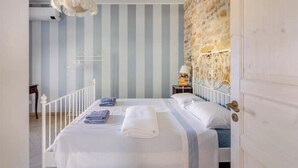 A bedroom with a bed, white curtains, a stone wall, and a white door.