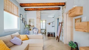 A living room with a sofa, wooden beams, a window, and a plant.