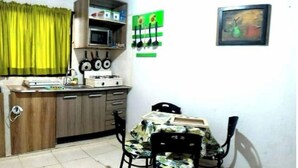 A compact kitchen with a microwave, stove, and cabinets. There is a dining table with chairs and a small window with curtains. - Yopal Apartment (Medellín)