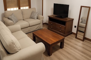 Una sala de estar con un sofá, una mesa de centro, un televisor sobre un mueble de madera y un espejo.