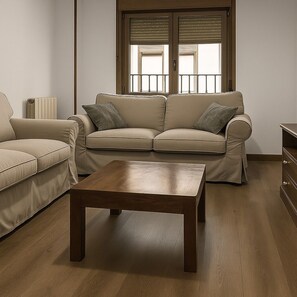 Una sala de estar con un sofá color beige, una mesa de centro de madera y un radiador.