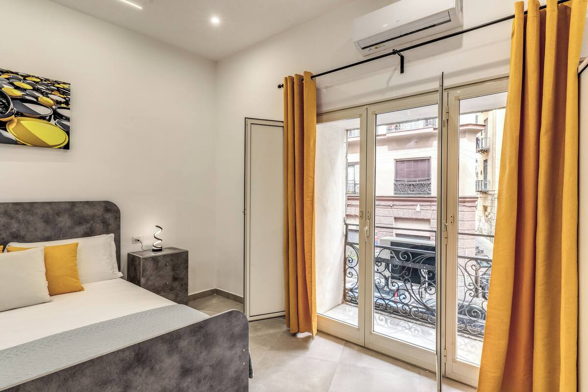 Ein Schlafzimmer mit einem Bett, einem Nachttisch, einer Wand-Klimaanlage und einer Glastür zum Balkon.