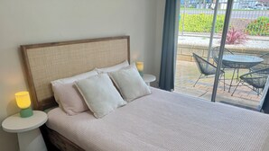 A neatly made bed with a wooden headboard and two pillows, a bedside lamp, and a view of an outdoor patio with chairs and a table. - Modern, fully equipped, and pet-friendly accommodation. (Port Lincoln)