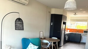 A modern living room with a blue armchair, a small round table, and a dining area with a white chair. - Modern, fully equipped, and pet-friendly accommodation. (Port Lincoln)