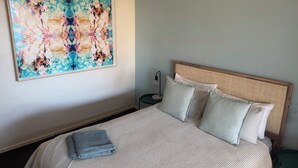 A neatly made bed with a patterned bedspread and pillows, a wall-mounted abstract painting, and a bedside table with a lamp. - Modern, fully equipped, and pet-friendly accommodation. (Port Lincoln)
