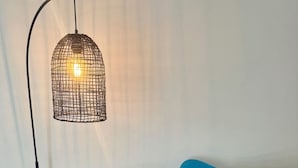 A blue sofa with a matching ottoman, a teal throw blanket, and a decorative pillow. A floor lamp with a woven shade is positioned above. - Modern, fully equipped, and pet-friendly accommodation. (Port Lincoln)