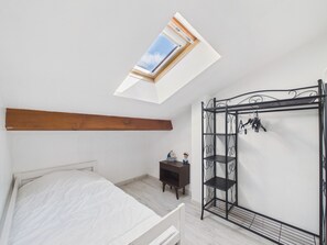 Un dormitorio con una cama litera, una mesita de noche, una repisa, una estantería y un tragaluz.