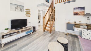 Un salon moderne avec un téléviseur, un escalier en bois et un panneau d’accueil.