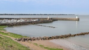 Un port de plaisance situé sur la côte, avec des bateaux amarrés, un phare et une digue rocheuse.
