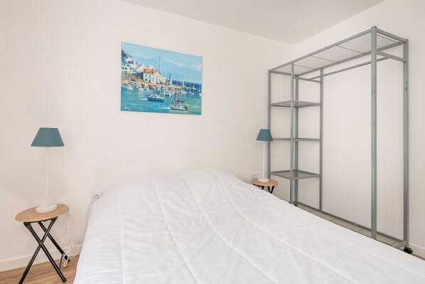 Un dormitorio con cama, un armario metálico, un cuadro de un puerto y dos lámparas.