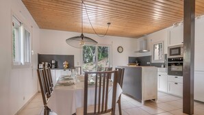 Une cuisine moderne avec des meubles blancs, un plafond en bois et un coin repas avec une table dressée pour quatre personnes.