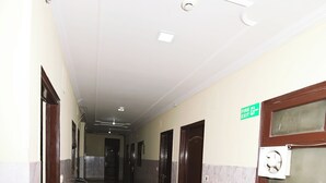 A hallway with marble flooring, doors, and a fire exit sign. - Hotel Jindal  (New Delhi)