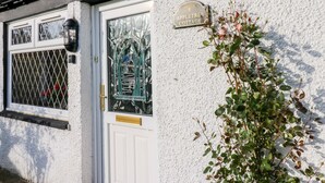 Un cottage bianco con un cancello in metallo, una finestra con decorazioni in vetro e un cartello che dice 'Apple Tree Cottage'.