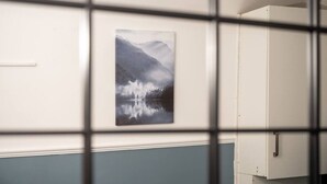 Una stanza con un dipinto incorniciato raffigurante un lago e montagne, un armadietto bianco e una parete blu.