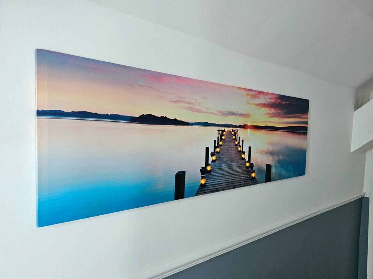 Een lange gang met een groot schilderij aan de muur, waarop een zonsondergang boven het water is afgebeeld.