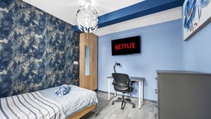 Una camera da letto con un letto, una scrivania, una sedia, un armadio e una TV a parete che mostra "NETFLIX".