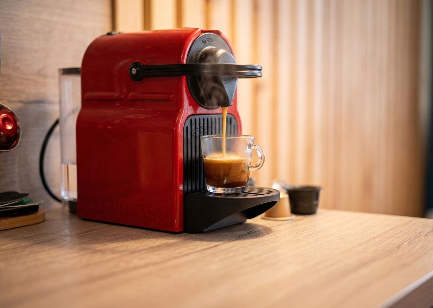 Una máquina de espresso roja sobre una encimera de madera, sirviendo café en una taza de vidrio.