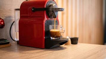 A red espresso machine on a wooden countertop with a glass cup of coffee being dispensed.