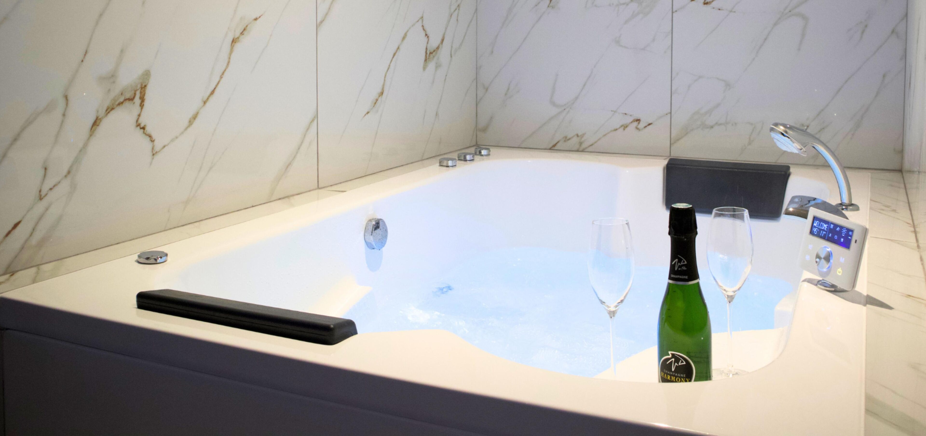 Een moderne badkamer met een marmeren wand, een ligbad, een fles wijn en een wijnglas.