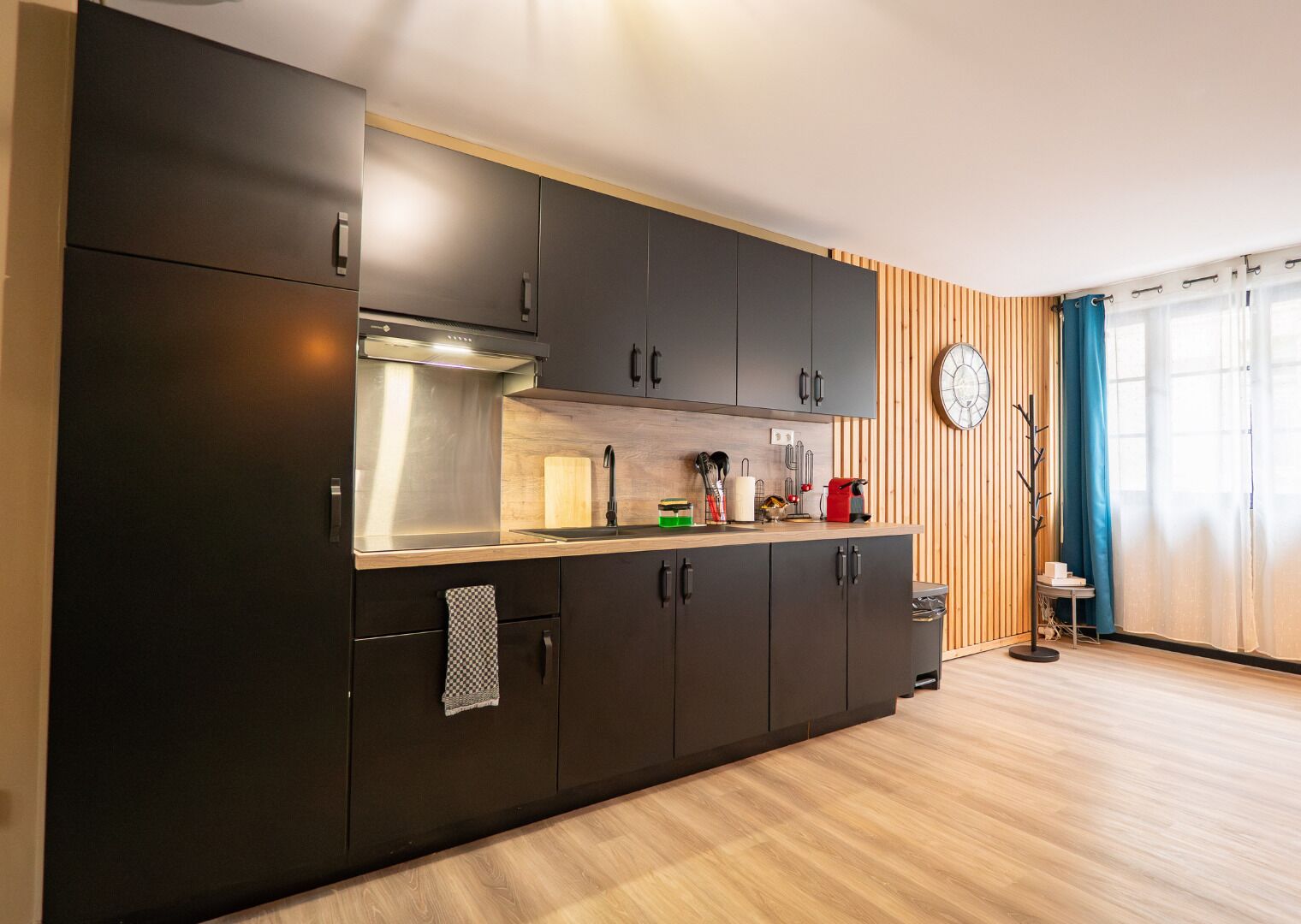 A modern kitchen with dark cabinets, a stainless steel range hood, and a wooden countertop.