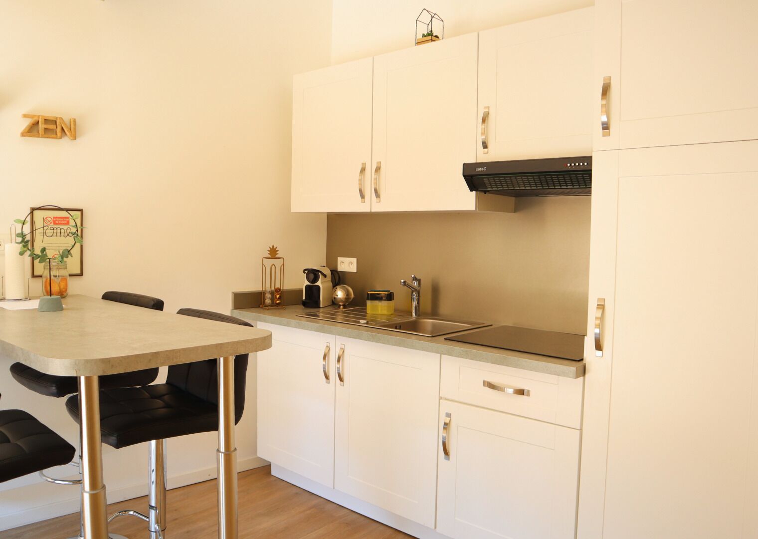 A compact kitchen with white cabinets, a black range hood, and a small dining area with a table and chairs.