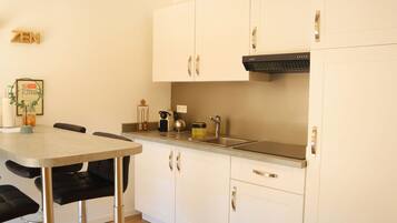 A compact kitchen with white cabinets, a black range hood, and a small dining area with a table and chairs.