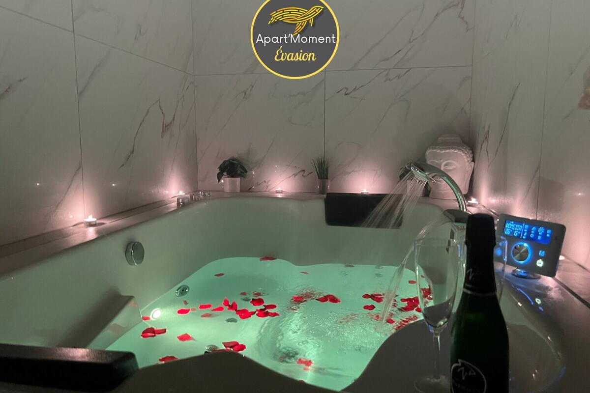 A modern bathroom with a jacuzzi, rose petals on the floor, a bottle of champagne, and a digital control panel.
