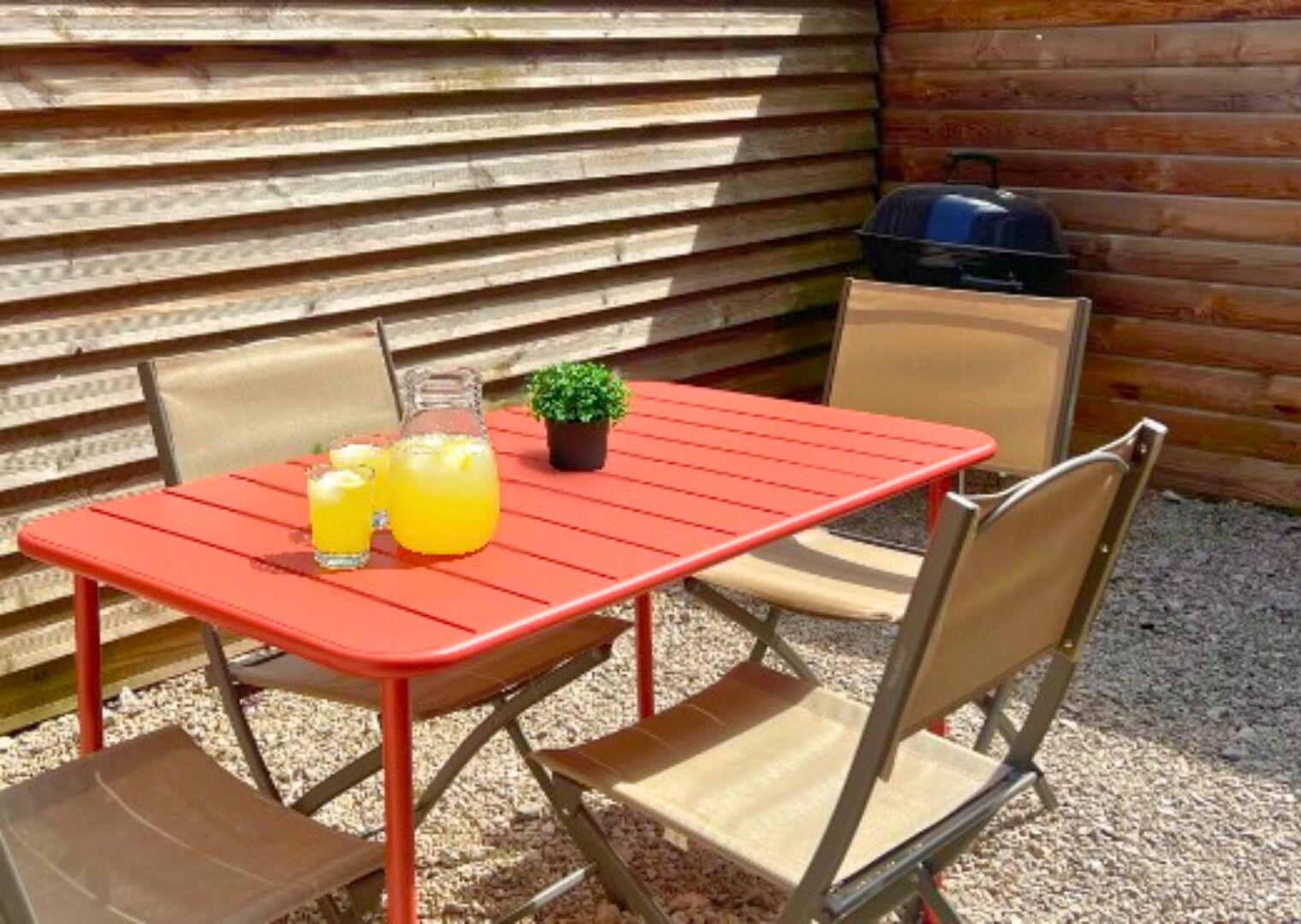 Ein roter Metalltisch mit vier Stühlen, einem kleinen Topfpflanzen und zwei Gläsern Orangensaft.