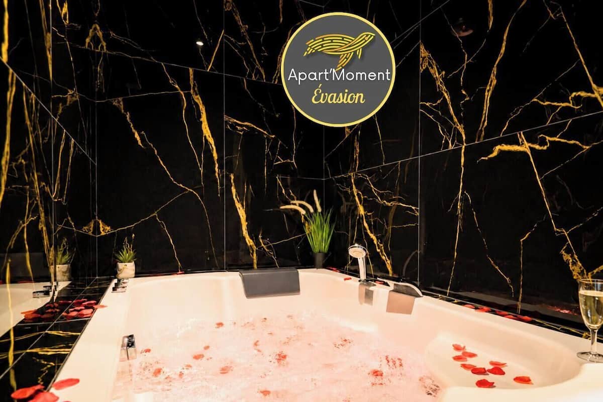A luxurious bathtub with rose petals, a champagne bottle, and glasses on the side.