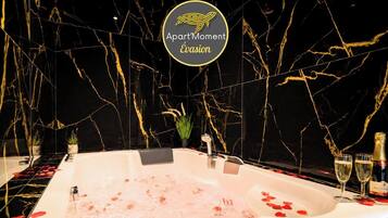 A luxurious bathtub with rose petals, a champagne bottle, and glasses on the side.