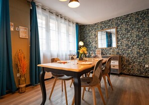 A dining area with a wooden table, chairs, a vase with flowers, and a mirror on the wall. - Apart'Moment ÉVASION (Saint-Omer)