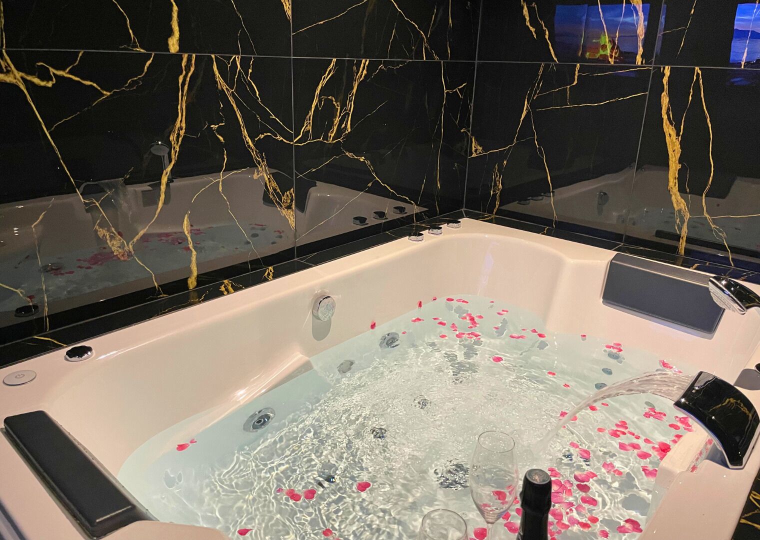 Ein modernes Badezimmer mit einer Marmorwand, einer mit Wasser und Rosenblättern gefüllten Badewanne und einem Smartphone am Badewannenrand.