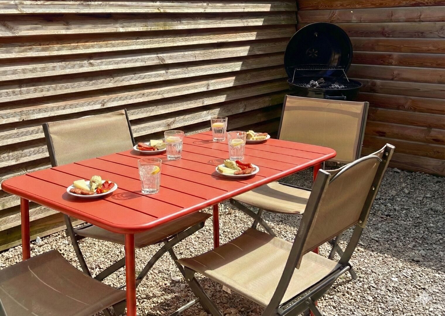 A red metal table with four chairs, a grill, and plates of food and drinks.