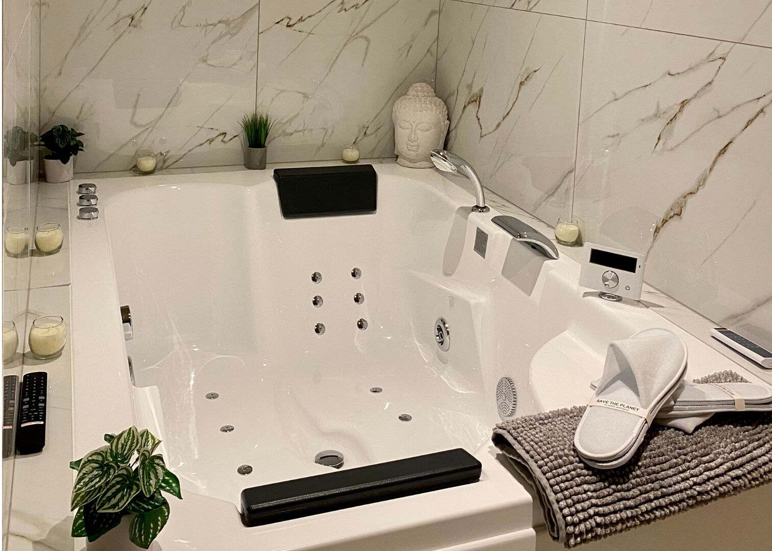 Een moderne badkamer met een ruime badkuip, een handdouche, een inbouwkrukje en een kleine potplant.