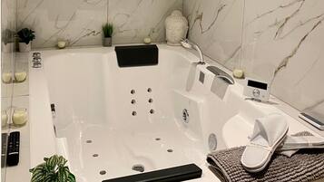 Een moderne badkamer met een ruime badkuip, een handdouche, een inbouwkrukje en een kleine potplant.