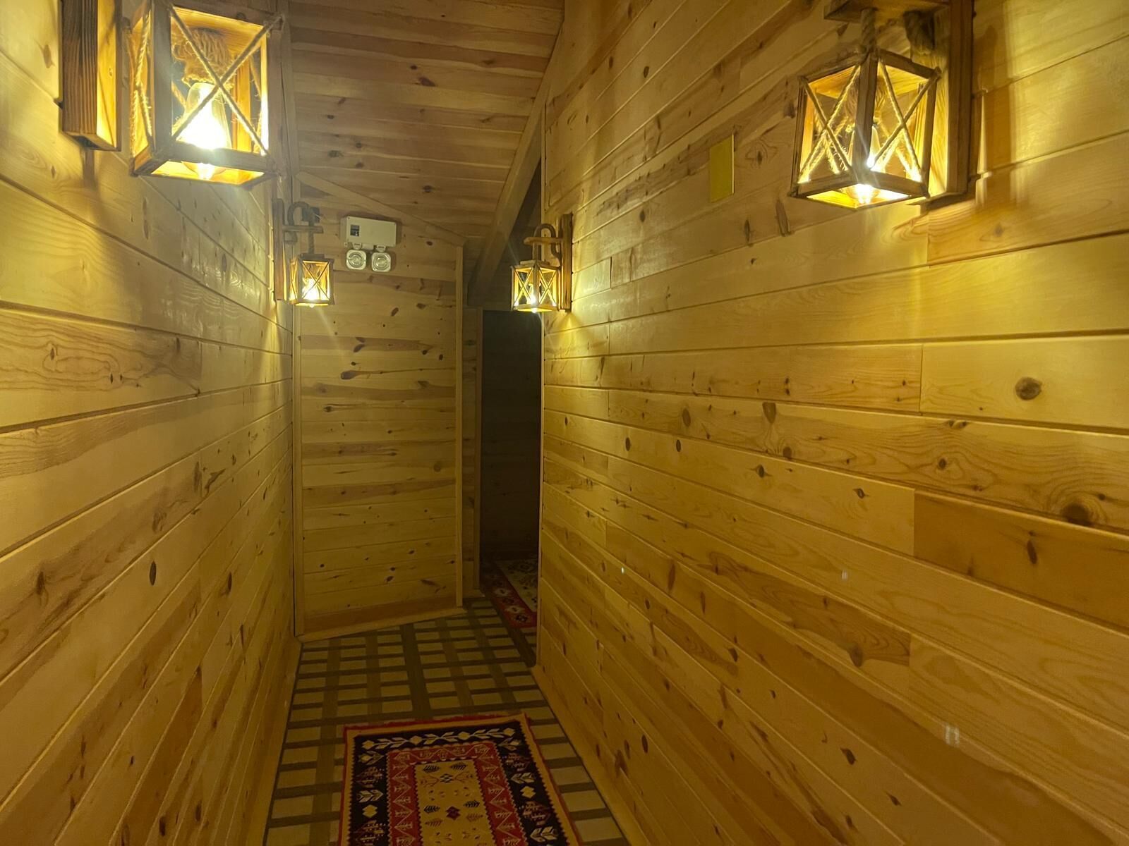 Un estrecho pasillo de madera con lámparas tipo farol en las paredes y un tapete con diseño en el suelo.