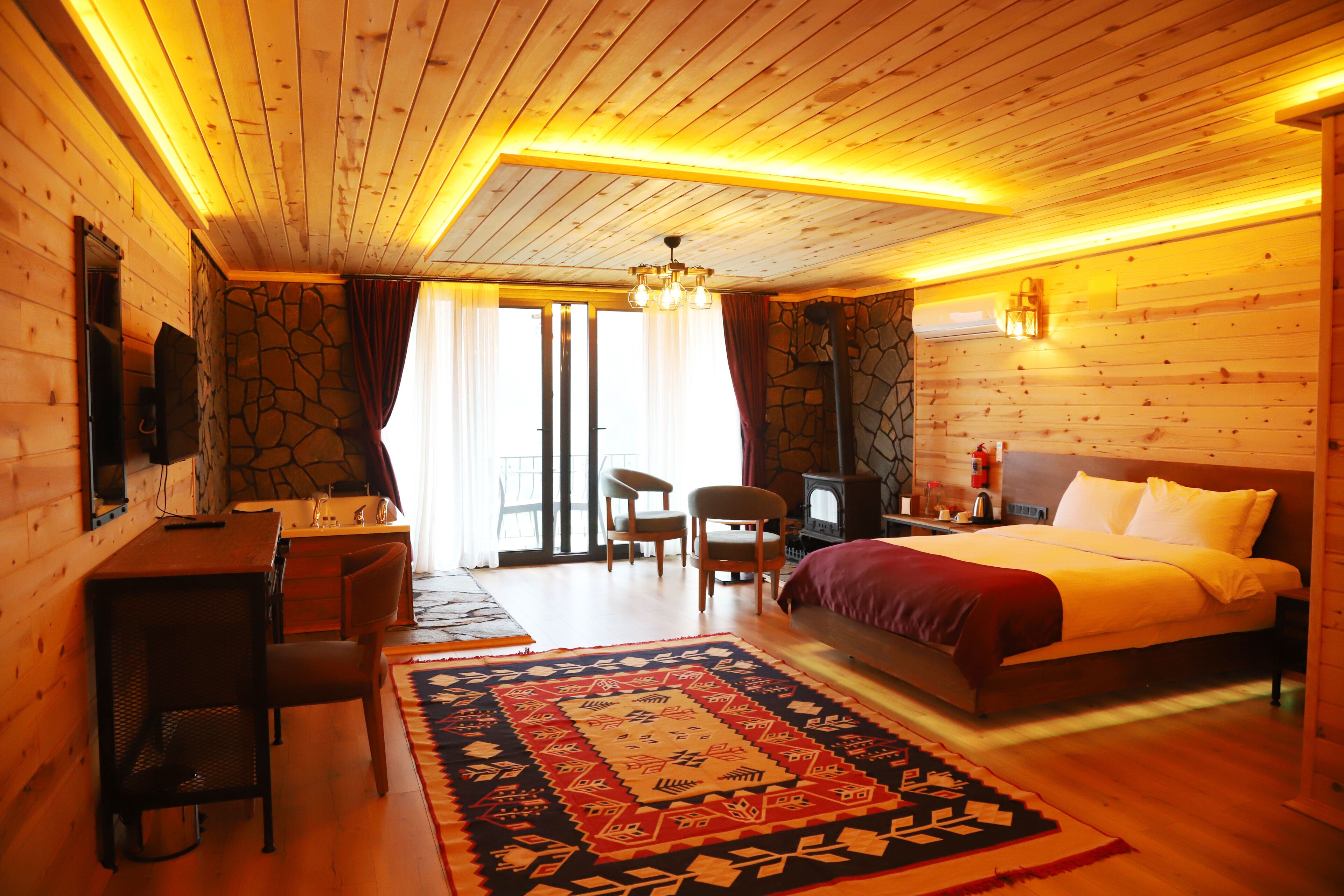 A cozy wooden room with a bed, a desk, and a stone wall.