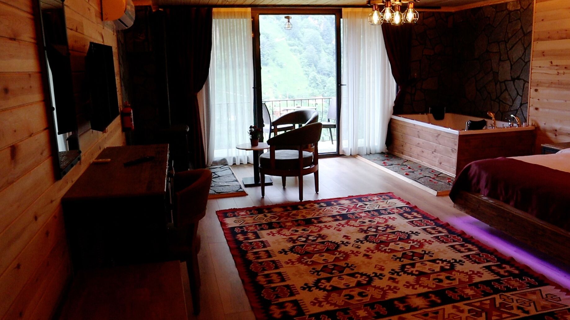 A wooden room with a bed, a desk, a chair, and a large window.