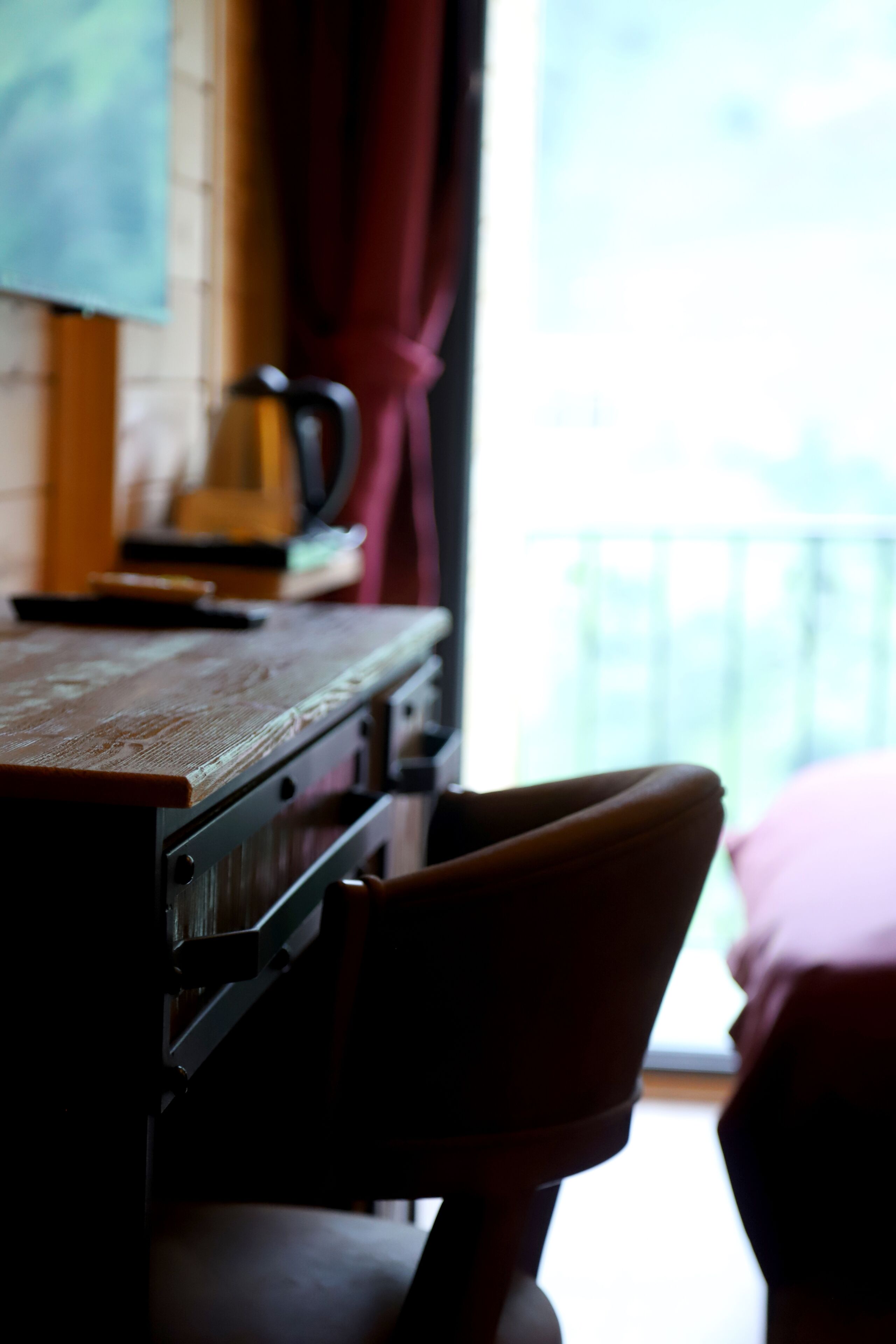 A room with a wooden desk, a chair, a window with curtains, and a view of the outside.