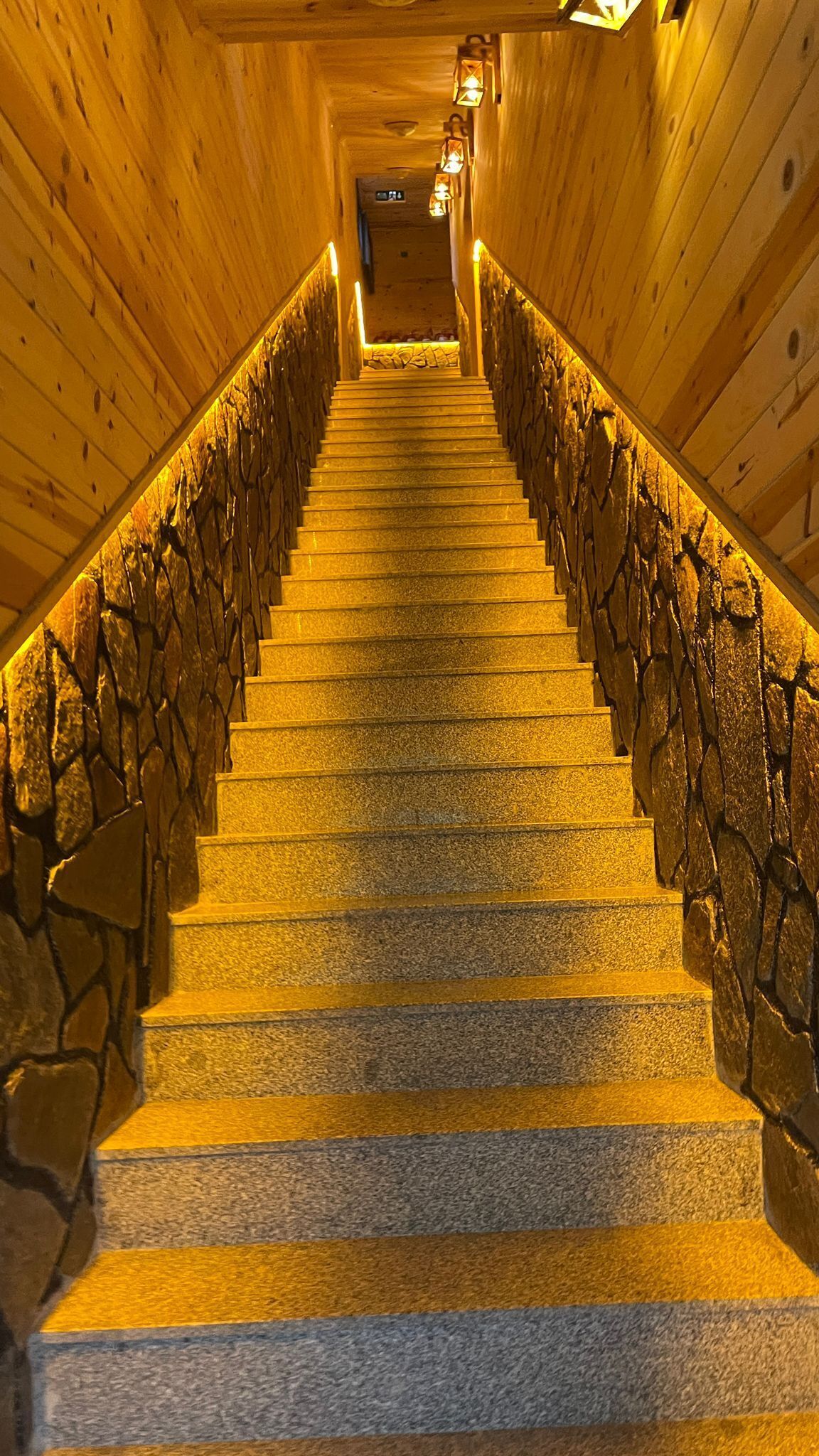 Una escalera de madera con paredes de piedra e iluminación cálida.