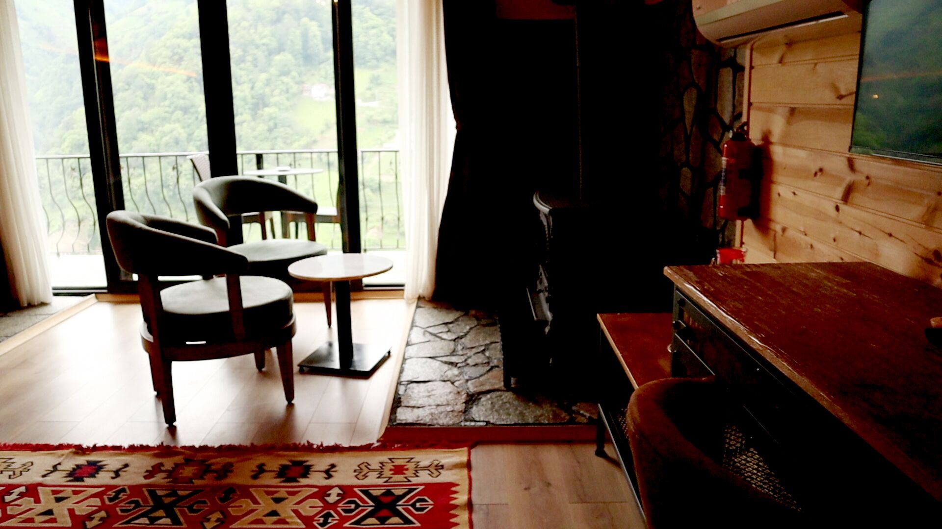 A cozy room with a wooden floor, a small round table, two chairs, a red sofa, and a TV on the wall.