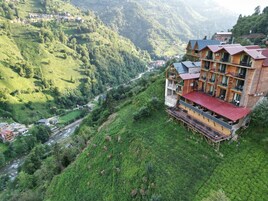 Un edificio de madera de varios pisos con balcones, ubicado en una ladera con un río al fondo.
