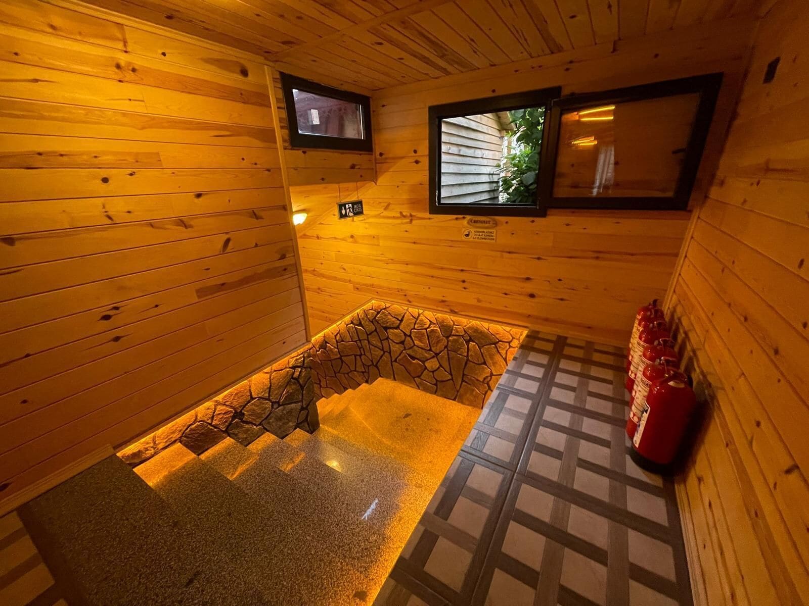 L’intérieur d’un chalet en bois, avec une cheminée en pierre, un petit téléviseur fixé au mur et un plancher carrelé.