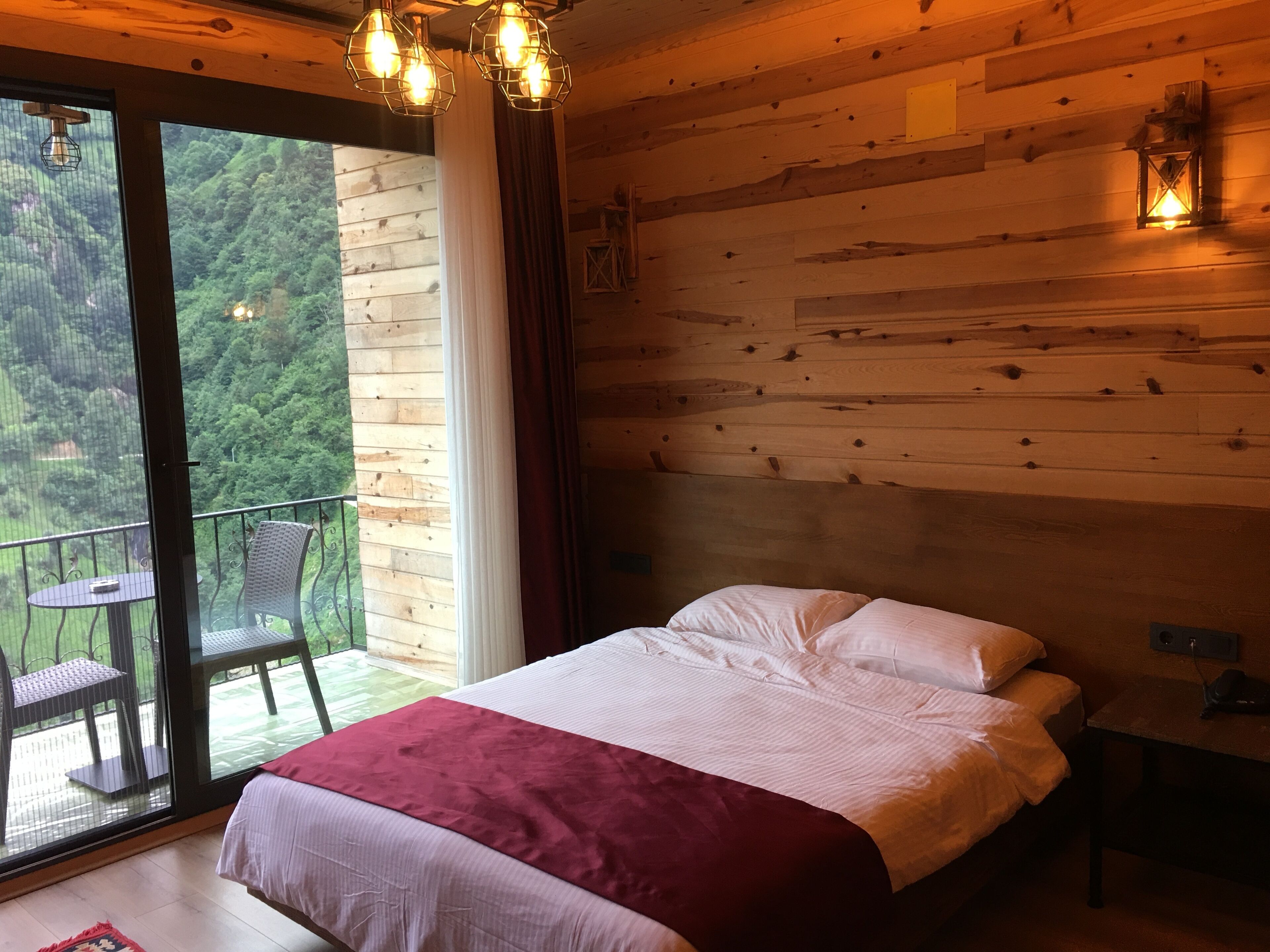 A bedroom with a large bed, a balcony with a table and chairs, and wooden walls.